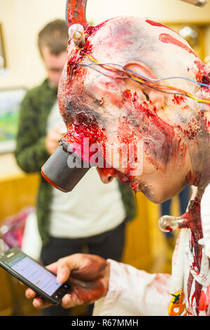Portrait of a tired white-collar worker who became zombie, talking on his phone wearing a black suit, with blood on his face standing against black br Stock Photo