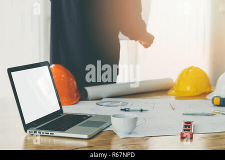 Empty blank screen laptop with a cup of coffee and blueprint on wooden table in office with Architect background Stock Photo