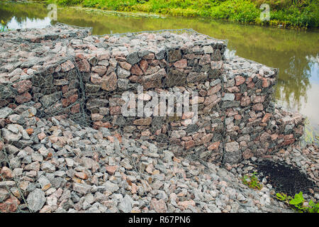 Texture for the background backdrop freely lying stone supported by a metal mesh. Technology of construction of fences from natural materials. Element of landscape design for architecture Stock Photo