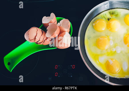 Flat lay above egg and eggshells on the kitchen a green spoon on an electric black plate with natural light. Stock Photo