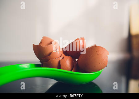 Flat lay above egg and eggshells on the kitchen a green spoon on an electric black plate with natural light. Stock Photo