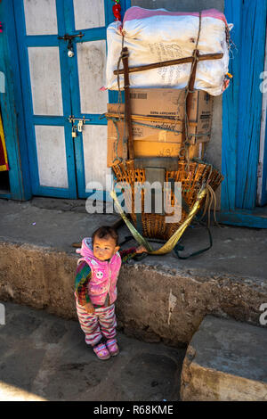 Nepal, Lukla, small child below large load to be carried by porter to Namche Bazaar Stock Photo