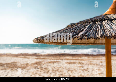 Close up shot with shallow depth of field of a straw made tropical beach umbrella in front of a defocussed turquoise sea. Stock Photo