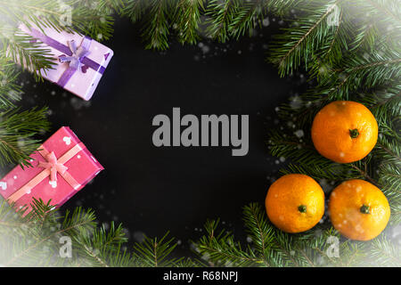 Frame of snow-covered fir branches, orange mandarins, gift boxes with dark copy space in middle. Stock Photo