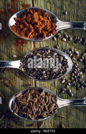 Spoons of cumin, cayenne peppers and chia seeds on a wooden background Stock Photo