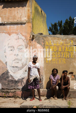 Young women in front of her house with an old Communist propaganda wall painting of Leonid Brejnev, Huila Province, Vilhambundu, Angola Stock Photo