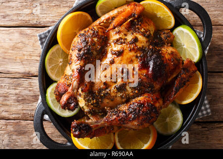 Citrus whole baked chicken served with fresh oranges and limes close-up in a frying pan on the table. horizontal top view from above Stock Photo