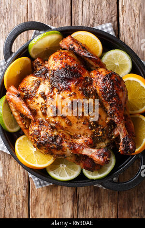 Citrus whole baked chicken served with fresh oranges and limes close-up in a frying pan on the table. Vertical top view from above Stock Photo