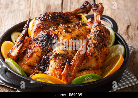 Citrus whole baked chicken served with fresh oranges and limes close-up in a frying pan on the table. horizontal Stock Photo