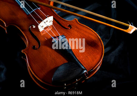 Vintage brown  violin with violin arc on a black fabric background, close up, still life Stock Photo