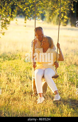 Portrait, Outdoor, Ganzfigur, aelteres Paar im Park, die Frau sitzt auf einer Schaukel Stock Photo