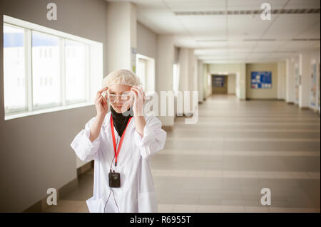 woman in overalls. employee wears protective glasses, wearing a white robe and a protective cap, earphone in the ear. Industrial production in the territory of the enterprise Stock Photo