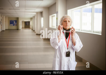 woman in overalls. employee wears protective glasses, wearing a white robe and a protective cap, earphone in the ear. Industrial production in the territory of the enterprise Stock Photo