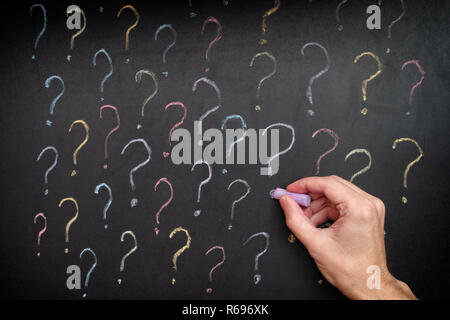 Man drawing colorful question marks on blackboard. Close up. Stock Photo