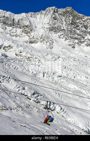 Skiers On A Chairlift Against The Fee Glacier And The Peak Dom, Mischabe Stock Photo