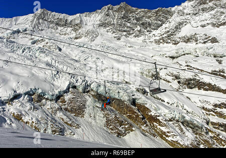 Skiers On A Chairlift Against The Fee Glacier And The Mischabel Massif, Saas-Fee, Switzerland Stock Photo