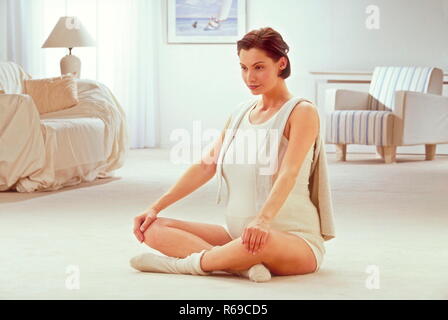Portrait, hochschwangere Frau sitzt auf dem Boden ihres Wohnzimmers und macht Schwangerschaftsgymnastik Stock Photo