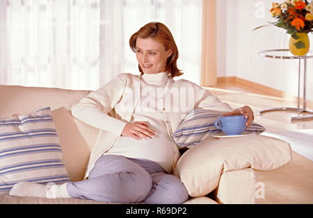Portrait, schwangere Frau sitzt entspannt auf einem weissen Sofa Stock Photo