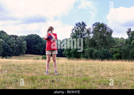 A teenage girl in a red T-shirt taking a photograph using a plastic 35mm film camera Stock Photo
