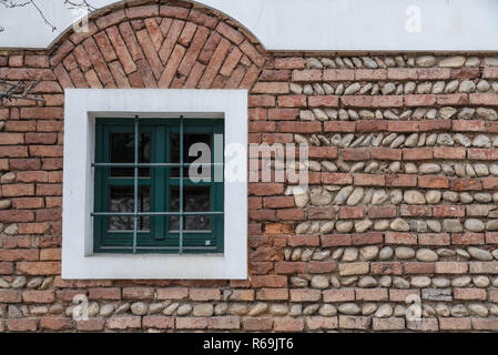 Windows With Window Bars In The Middle Of A Brick Wall Of Bricks And Boulders Stock Photo
