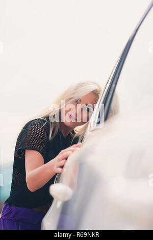 Cheerful young female driver hugging her new car. Stock Photo
