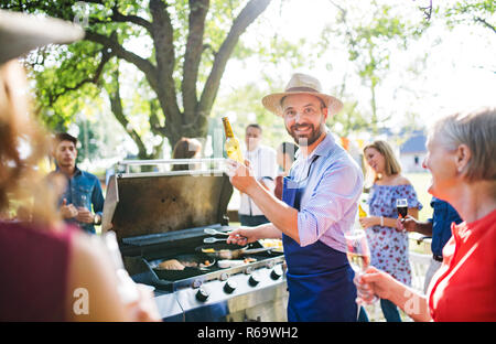 A mature man with family and friends cooking and serving food on a barbecue party. Stock Photo