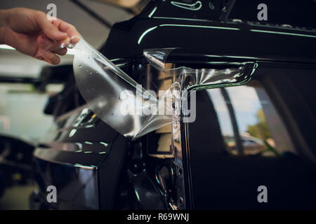 Worker hands installs car paint protection film wrap. Stock Photo