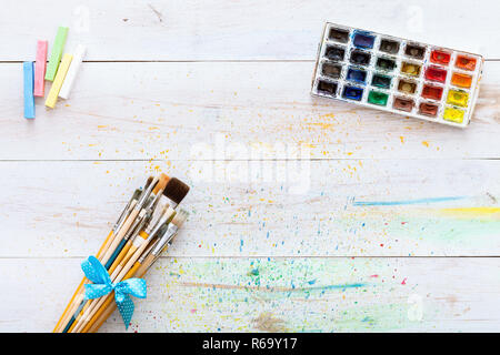 Paint brushes set and box with watercolors on white wooden stained table with splashes, artistic background for creative work, children kids easy pain Stock Photo