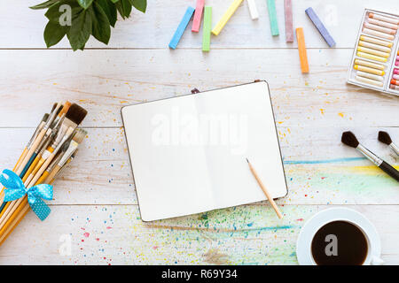 Creative art designer workplace, artistic mock up, blank notebook for sketches with pencil on it, set of paintbrushes and cup of coffee on white woode Stock Photo