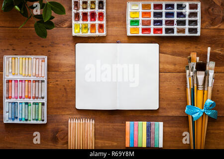 https://l450v.alamy.com/450v/r69y8m/creative-art-work-accessory-supplies-set-open-notebook-for-sketch-paint-brushes-paintbox-with-watercolors-crayons-pencils-on-brown-wooden-artisti-r69y8m.jpg