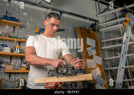 A carpenter works on woodworking the machine tool. Saws furniture details with a circular saw. Process of sawing parts in parts. Against the background of the workshop Stock Photo