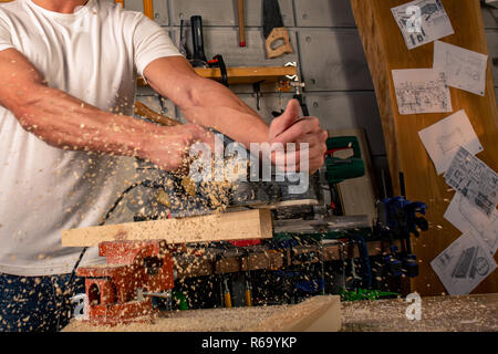 A carpenter works on woodworking the machine tool. Saws furniture details with a circular saw. Process of sawing parts in parts. Against the background of the workshop Stock Photo