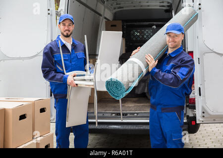 Two Delivery Men Holding Chairs And Carpet Stock Photo