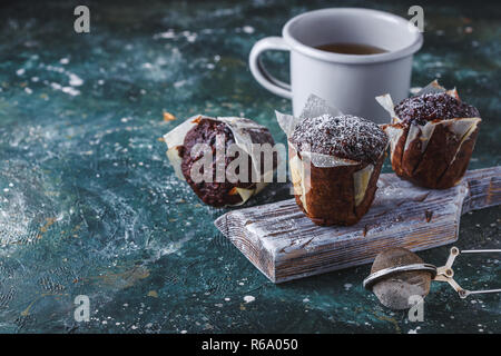Homemade Carrot-chocolate muffin dusted with icing sugar with a cup of tea on a dark table Copy space Stock Photo