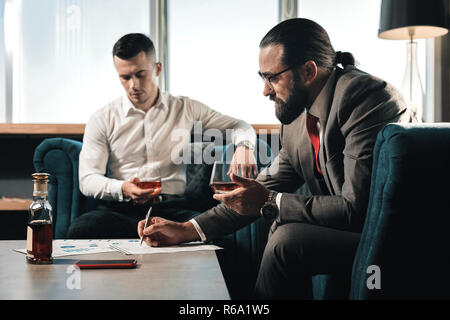 Two business partners drinking whisky and filling the documents Stock Photo