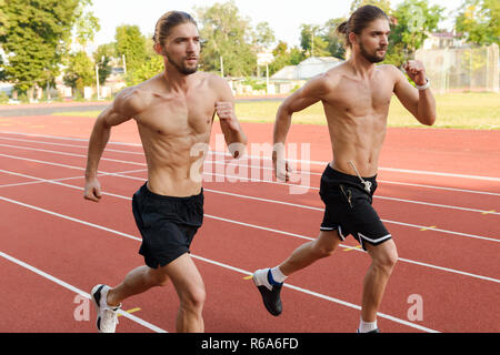 Photo of young strong two twins sportsmen brothers running at the stadium outdoors. Stock Photo