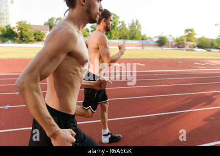 Photo of young strong two twins sportsmen brothers running at the stadium outdoors. Stock Photo