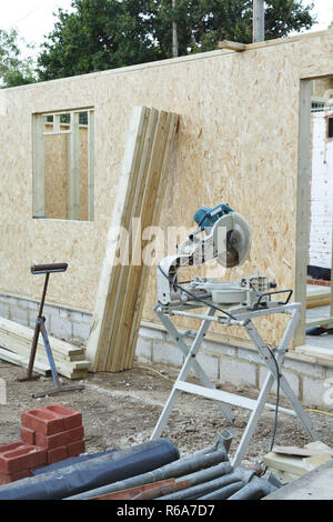 Carpenter's chop saw and timber with a timber framed house under construction in the background Stock Photo