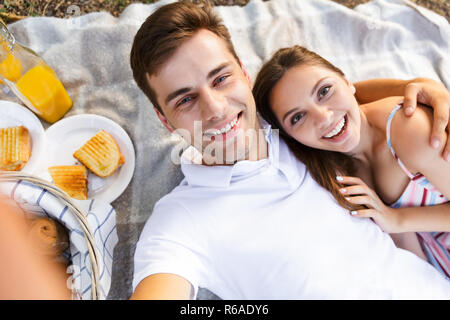 Happy young couple spending good time together, having picnic at the park, taking a selfie Stock Photo