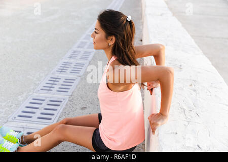 Photo of beautiful sporty woman 20s in tracksuit doing sit-ups, during workout at seaside Stock Photo