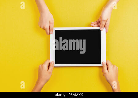 Two kid hands holding tablet computer over yellow background. Stock Photo