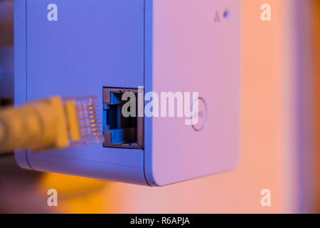 Insert ethernet cable into WiFi extender device which is in electrical socket on the wall Stock Photo