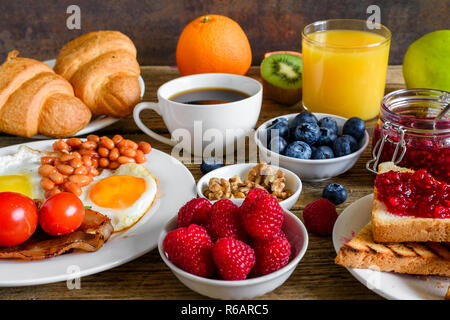 Breakfast including coffee, fried egg ,bacon, beans, croissant, orange juice with nuts, fruits and berries. close up Stock Photo