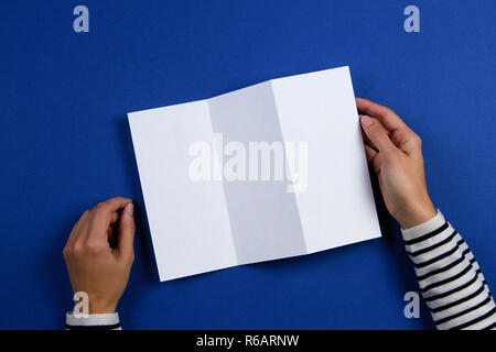 Woman hands holding blank white flyer brochure booklet. Mockup sheet template advertising booklet on blue background Stock Photo