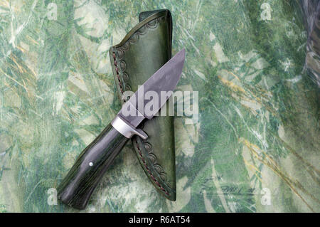 A hand forged knife and sheath displayed on top of camo fabric. Stock Photo