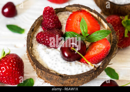 chia seeds pudding made of greek yogurt, berries and mint in coconut bowl over white wooden table. healthy breakfast. close up Stock Photo