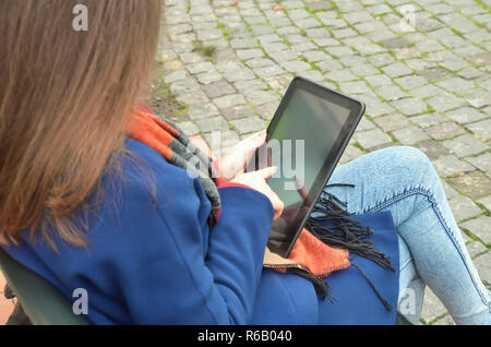 A woman is seated on a bench and uses a black tablet Stock Photo