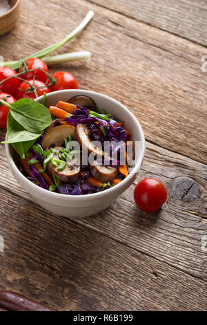 Stewed vegetables bowl. Plant based colorful vegetarian dish with spinach, red cabbage, mushrooms, bell pepper and carrot on rustic wooden table Stock Photo