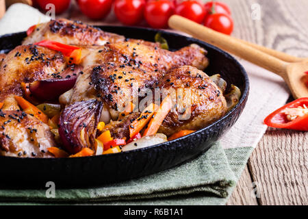 Roasted chile miso  chicken drumsticks  with vegetables in cast iron skillet on rustic wooden table close up, selective focus Stock Photo