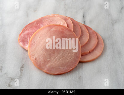 Several round breakfast ham slices on a marble cutting board. Stock Photo